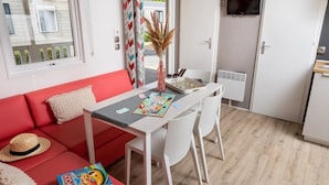 Una habitación acogedora con un sofá rojo, una pequeña mesa de comedor con sillas y un televisor montado en la pared.