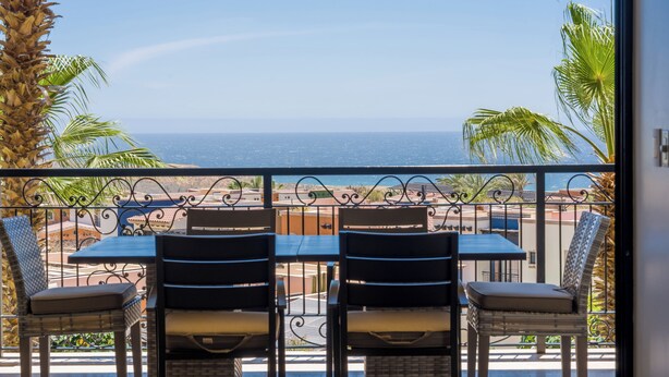 Een balkon met een tafel en stoelen, met uitzicht op de kust.
