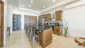 Een ruime keuken met een centraal eiland, barstoelen, houten kastjes en een grote koelkast.