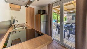 A compact kitchen with a sink, wooden cabinets, and a built-in microwave. - ZEcamping 3* animé piscine chauffée locatif TV LV clim 35m2 (Hauterives)