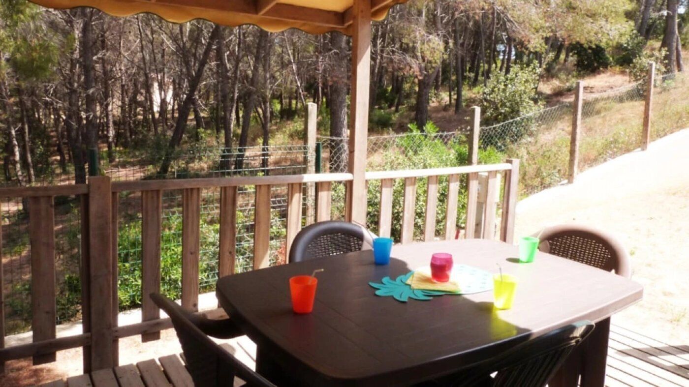 A wooden deck with a table and chairs, surrounded by a wooden railing and a wire fence.
