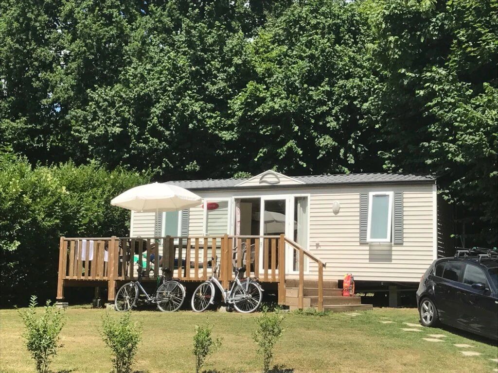 A mobile home with a porch, a bicycle, and a car parked in front.