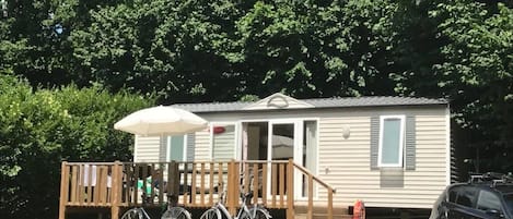 A mobile home with a porch, a bicycle, and a car parked in front.