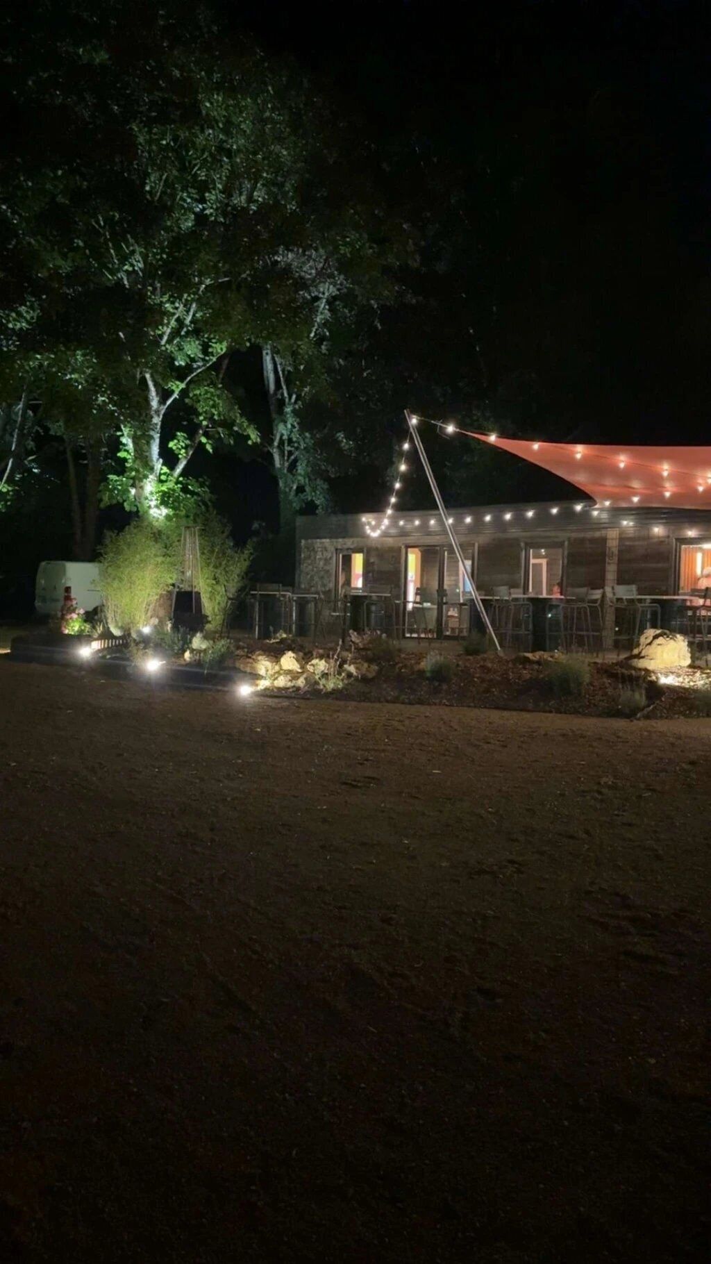 A building with a covered outdoor seating area, string lights, and a tree in the foreground.