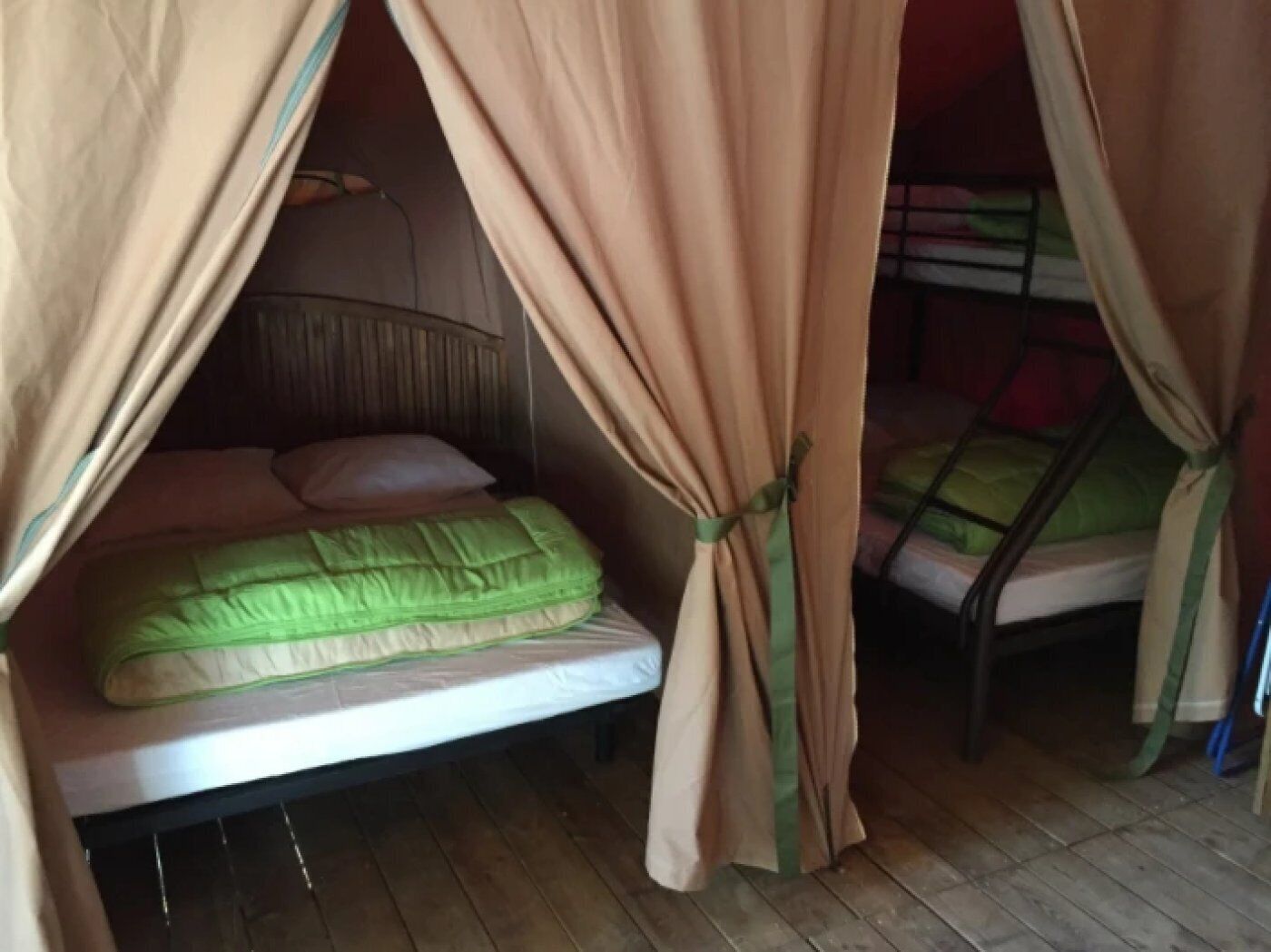 Una cama individual con colchón verde y cabecera, cubierta por un dosel color beige.