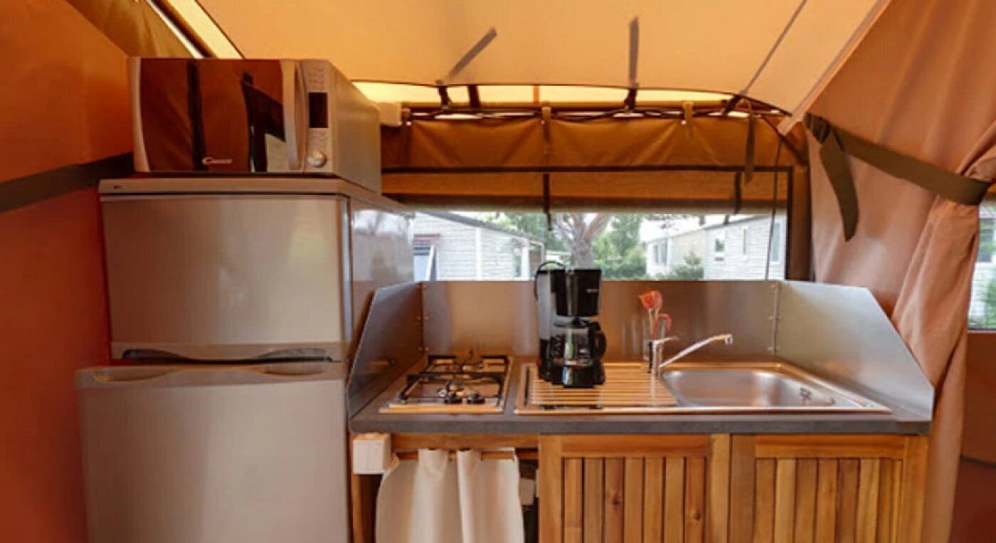 A compact kitchen with a refrigerator, stove, sink, and a coffee maker.