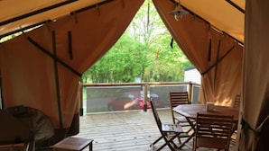 Ein überdachter Außenbereich mit Holzterrasse, einem Tisch mit Stühlen und einem Grill.