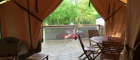 Et overdækket udendørsområde med træterrasse, et bord med stole og en grill.