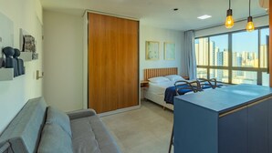 Een moderne hotelkamer met een bed, een bureau, een bank en uitzicht op de stad door grote ramen.