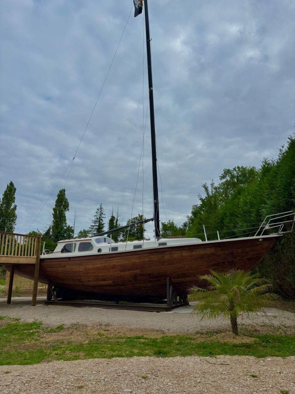 Een houten boot op een aanhanger in een grasrijk gebied, met bomen op de achtergrond.