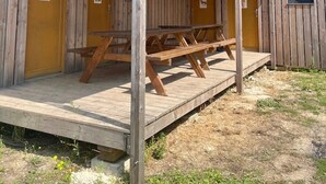 Uma cabana de madeira com varanda coberta, mesas de piquenique e duas portas amarelas.