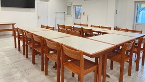 Uma sala de conferências com várias mesas e cadeiras, paredes brancas e uma grande televisão de tela plana na parede.