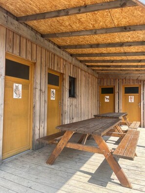 Un bâtiment en bois doté d’un espace extérieur couvert avec des sièges et de plusieurs portes ornées d’illustrations d’animaux.