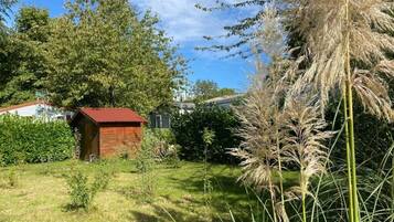 A rustic wooden cabin with a red roof, surrounded by lush greenery and tall grasses.