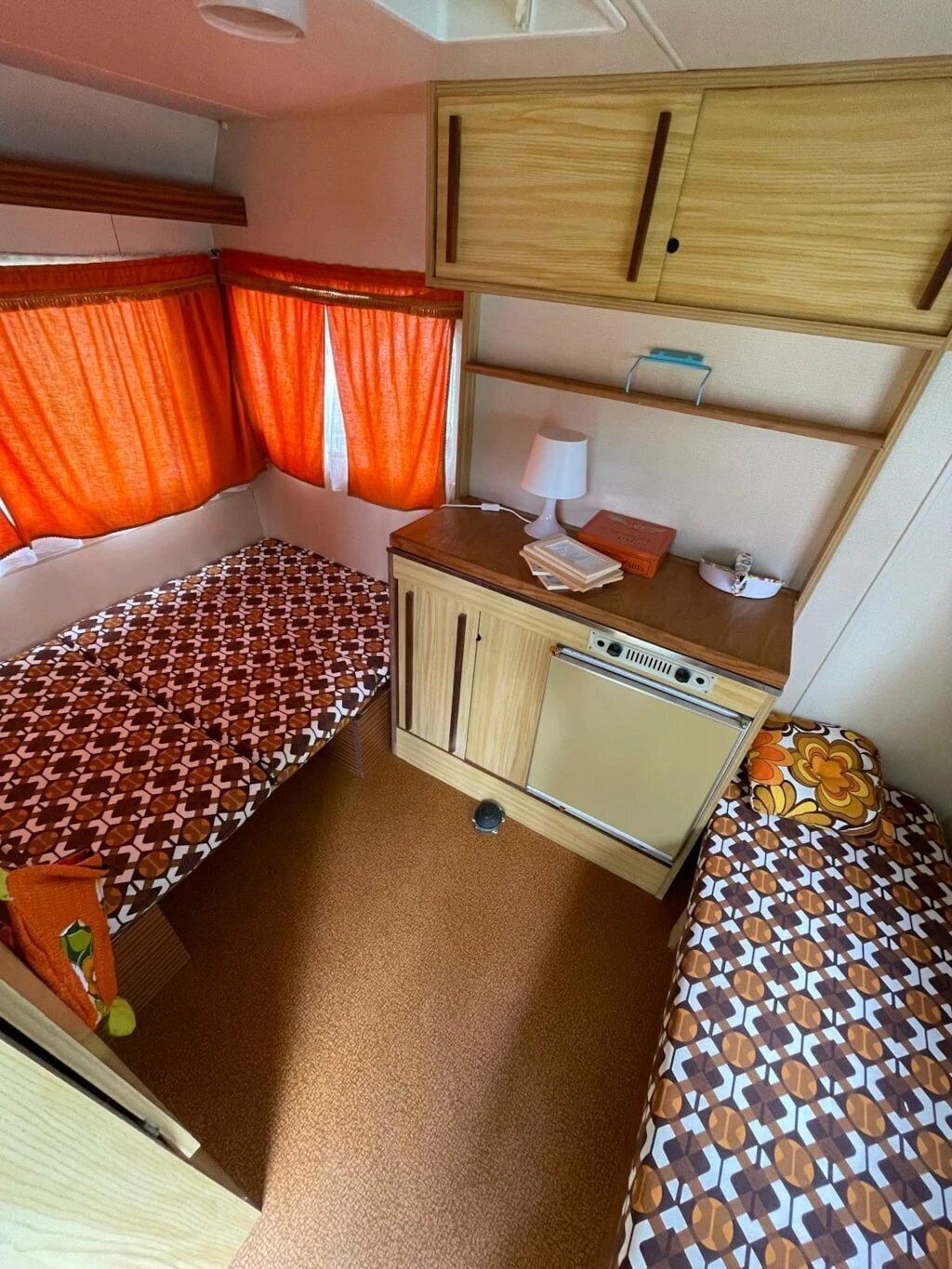 Un intérieur de camping-car compact comprenant deux lits, un coin cuisine et un petit espace salon.
