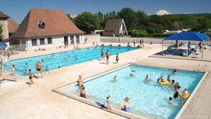 A swimming pool area with multiple pools, a covered seating area, and a building with a sloped roof. - ZEcamping 3 étoiles familial piscine chauffée locatif 16m2 2 pers (Hauterives)