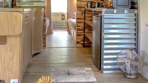 A compact kitchen with wooden cabinets, a refrigerator, and a microwave. There is a wooden table with a bowl of cherries and a glass of water. - ZEcamping 3 étoiles familial piscine chauffée locatif 16m2 2 pers (Hauterives)