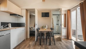 Een praktische keuken met een vaatwasser, een eethoek met tafel en stoelen, en een schuifdeur naar een douchegedeelte.