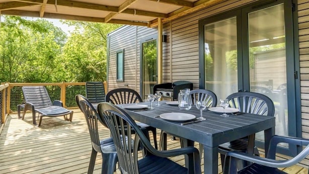 Een terras buiten met een eettafel, omringd door stoelen, en een barbecue op de achtergrond.