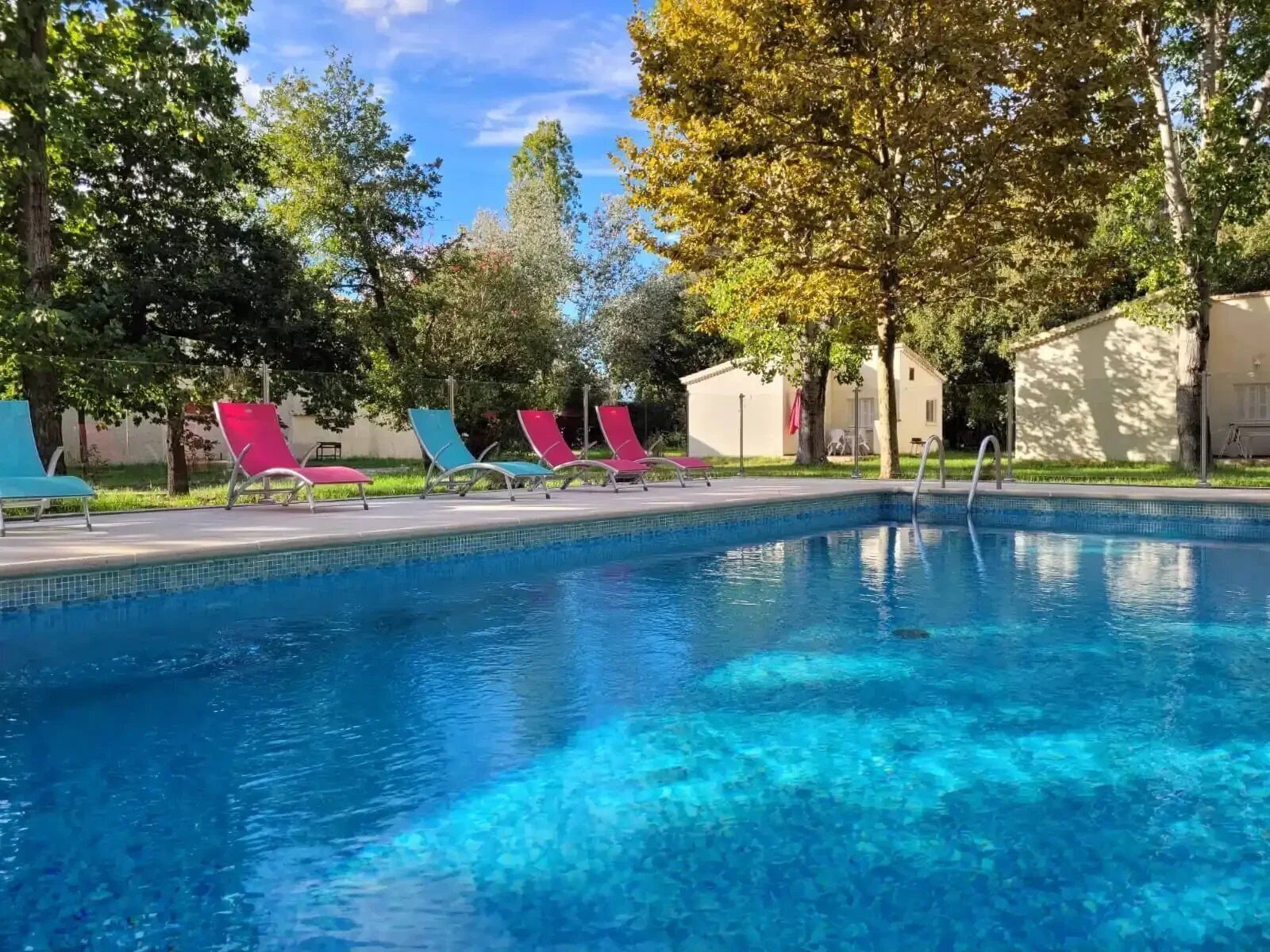 Piscina azul límpida com espreguiçadeiras e um edifício ao fundo.