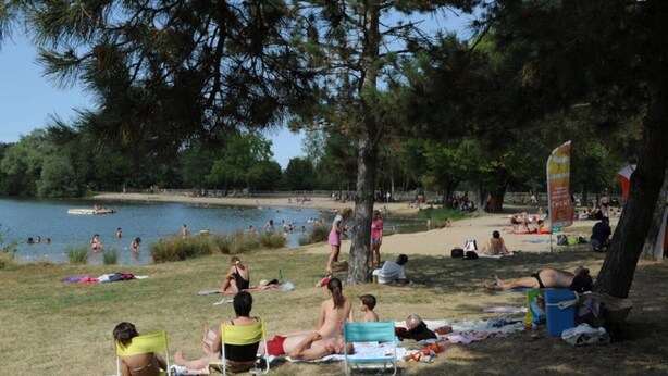 Un parque junto al lago, con gente descansando sobre el césped y a la orilla del agua.