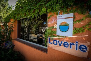 A building with a sign that reads "Laverie" and a window with a view of a garden. - ZEcamping 4* 3km plage piscine chauffée locatif TV clim 18m2 (Canet-en-Roussillon)