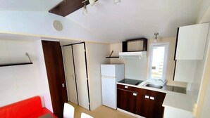 A compact kitchen with white cabinets, a microwave, and a refrigerator. There is a dining area with a brown table and white chairs. - ZEcamping 3 étoiles piscine pet friendly club enfant tente 27m2 4 pers (Sauxillanges)