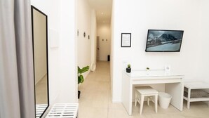 A modern, minimalist hotel room with a white desk, a small seating area, and a framed picture on the wall. - Valguarnera Studio Apartaments (Palermo)