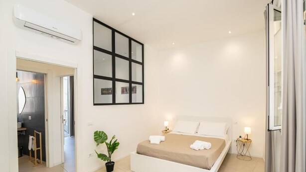 A modern bedroom with a large bed, a potted plant, and a wall-mounted TV. - Valguarnera Studio Apartaments (Palermo)