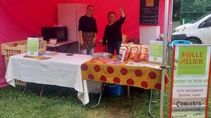 A food stall with a table covered in a white tablecloth and a yellow table runner with red polka dots. There are signs advertising 'Folle Allier guinguette' and 'BISTROT DE PLEIN AIR'.