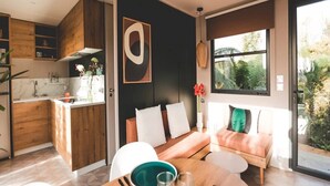 Une cuisine moderne avec des meubles en bois, un coin repas avec une table et des chaises en bois, un canapé avec des coussins et une grande fenêtre donnant sur un paysage verdoyant.