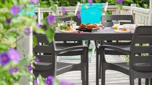 Une table à manger installée à l’extérieur, avec des chaises, un plateau de croissants et une nappe bleue.
