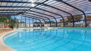 Une piscine intérieure dotée d’un toit en verre incurvé, entourée de chaises longues et d’une clôture blanche.