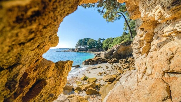 Une plage rocheuse offrant une vue dégagée à travers une arche naturelle.