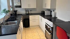 A modern kitchen with white cabinets, a stainless steel sink, a kettle, a toaster, and a red chair. - PapaJoe's Get-away! Just what you deserve
sleeps 8/2 toilets/6 min to Waterworld (Stoke-on-Trent)
