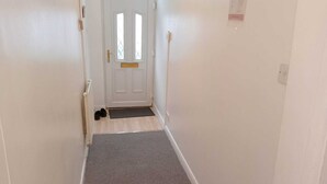 A narrow hallway with a white door at the end, a small mat at the entrance, and a light switch on the wall. - PapaJoe's Get-away! Just what you deserve
sleeps 8/2 toilets/6 min to Waterworld (Stoke-on-Trent)