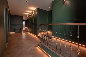Un interior moderno con piso de madera, paredes verdes y una escalera con un diseño único para la barandilla.