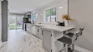 A modern kitchen with white cabinetry, a marble floor, and a large window. - Snowmobile-In Riverside Suite with Sauna, Marina, Sleeps 6! (Coldwater)