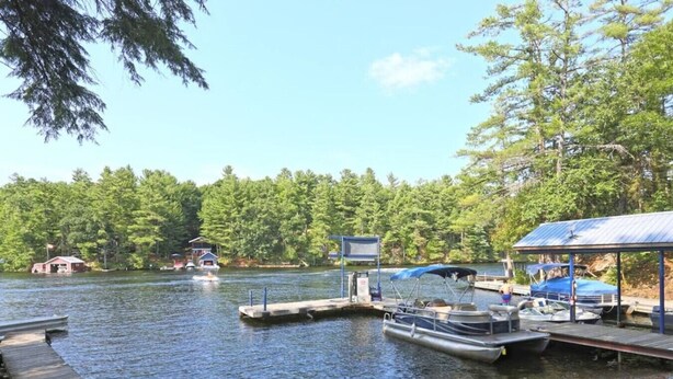 A dock with boats, a covered area, and a forested shoreline. - Snowmobile-In Riverside Suite with Sauna, Marina, Sleeps 6! (Coldwater)