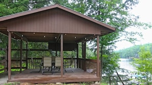 A wooden deck with chairs and a table, overlooking a river. - Snowmobile-In Riverside Suite with Sauna, Marina, Sleeps 6! (Coldwater)