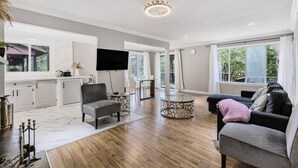 A spacious living area with a wooden floor, a grey sofa, a round glass coffee table, and a flat-screen TV mounted on the wall. - Snowmobile-In Riverside Suite with Sauna, Marina, Sleeps 6! (Coldwater)