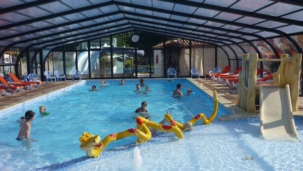 Ein Hallenbad mit klarem Wasser, einer Rutsche und Liegestühlen.