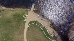 An aerial view of a lakeside property with a circular wooden deck, a pathway leading to a dock, and a grassy area with colorful chairs. - Summer Ready: Private 4BR Lakefront Cottage in Barry's Bay (Barry`s Bay)