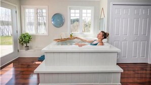 A person relaxing in a white hot tub in a room with large windows, a potted plant, and a door. - Summer Ready: Private 4BR Lakefront Cottage in Barry's Bay (Barry`s Bay)
