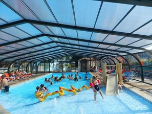 En inomhuspool med ett tak som delvis är öppet, vattenrutschkanor och avkopplande sittområden.