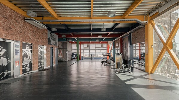 A spacious gym with exercise equipment, large windows, and a brick wall.