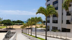 A modern building with a concrete facade, a series of palm trees, and a clear view of the beach in the background. - Beach Class #1104 - Quadruplo por Carpediem (Recife)