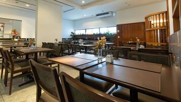 Un restaurante espacioso con varias mesas y sillas, un área de cocina al fondo y un diseño de interiores moderno.