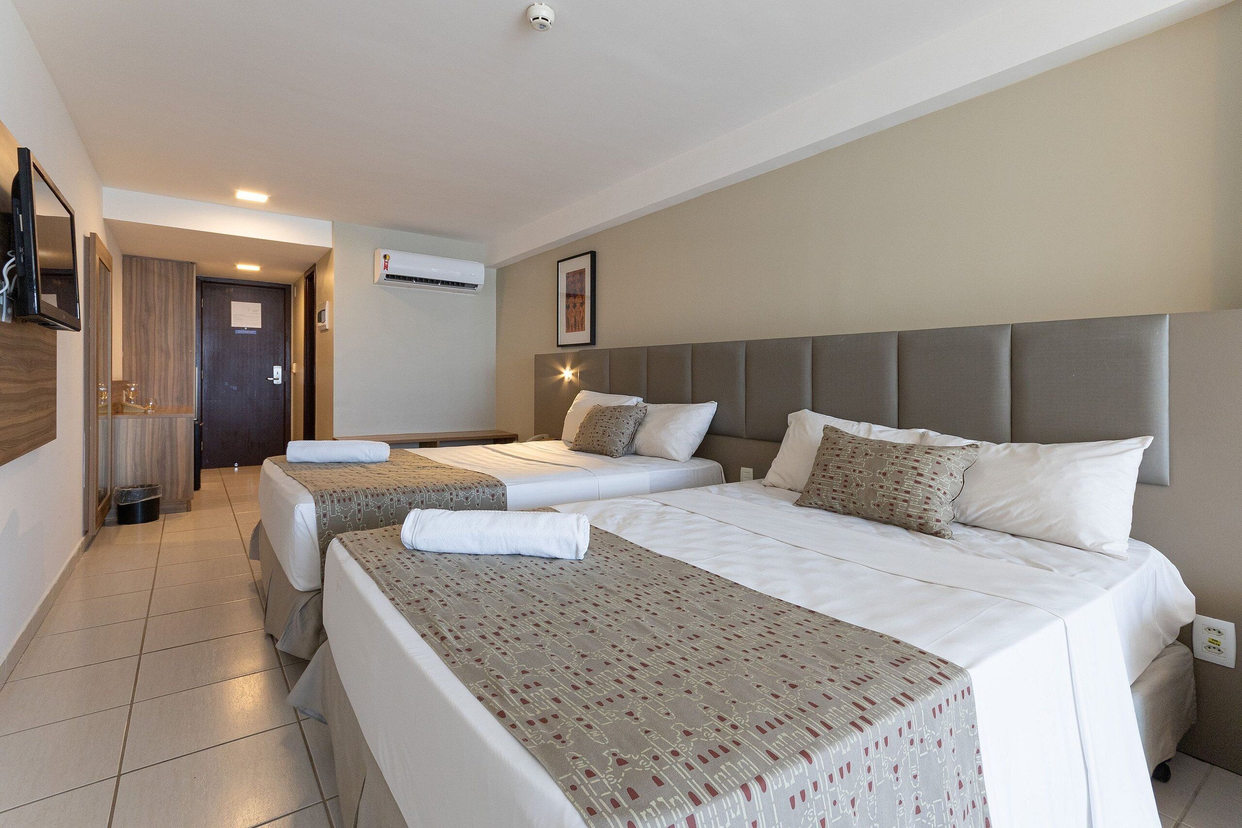 A hotel room with two beds, a TV, an air conditioning unit, and a framed picture on the wall.