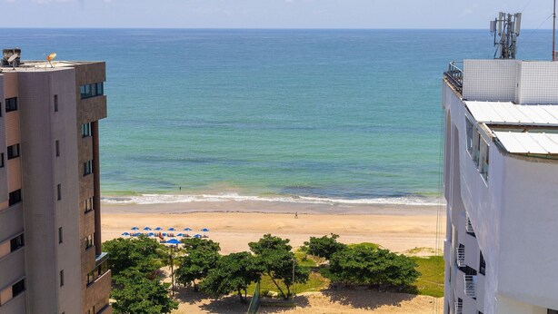A beach view from a building with a sandy beach, umbrellas, and trees. - Beach Class #1104 - Quadruplo por Carpediem (Recife)
